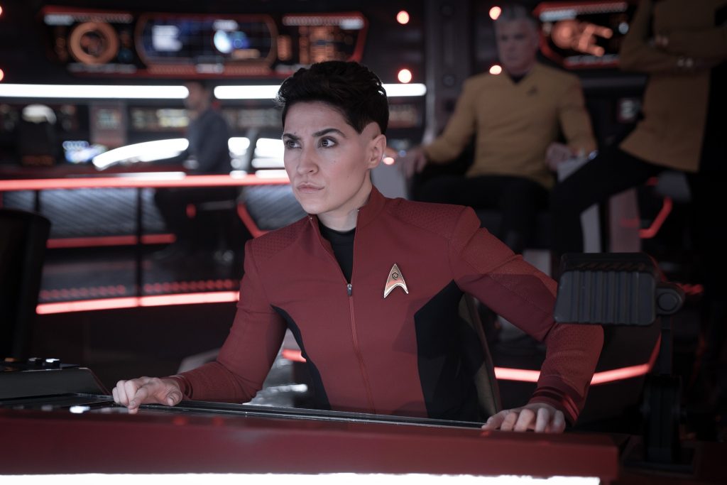 rica Ortegas (Melissa Navia) in uniforme rossa di Starfleet, concentrata davanti a un pannello di controllo sulla plancia di una nave.