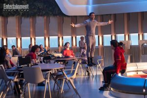 Sandro Rosta in piedi su una sedia con le braccia aperte, di fronte ad altri studenti.