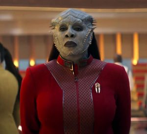 Primo piano della Comandante Lura Thok, un ibrido Klingon/Jem'Hadar, in uniforme rossa della Flotta Stellare con dettagli dorati.