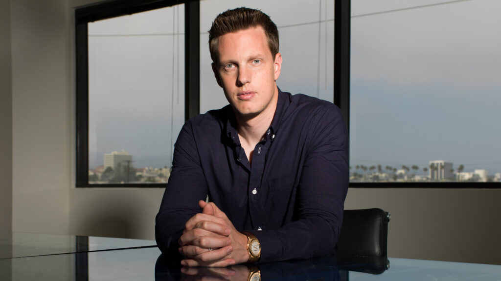 David Ellison, fondatore di Skydance Media, seduto a un tavolo con le mani giunte, di fronte a una grande finestra con vista sulla città.